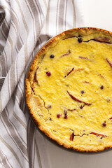 Delicious sweet cheese pie with apples and cranberries, fruit and berry curd pie on a white background with a kitchen towel, top view