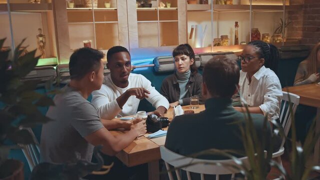 Young multiethnic group of friends talking and sharing secrets. People discussing interesting news hangout, diverse millennial students hanging in cafe together while having conversation and laughing