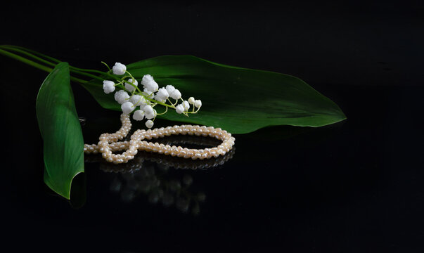 May lilies of the valley and a necklace of natural pink river pearls on a dark background.
