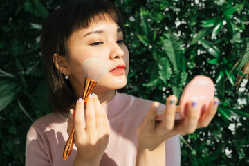 Asian thai woman apply cosmetic brush over green nature background outdoors.