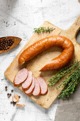 Smoked Cracow sausage on a wooden serving board on a light gray kitchen table. Slicing boiled and smoked sausage