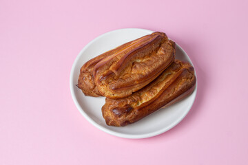 Eclairs on a pink background. Three eclairs on a white plate. Sweet breakfast.