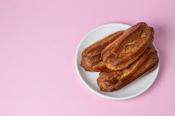 Eclairs on a pink background. Three eclairs on a white plate. Sweet breakfast.