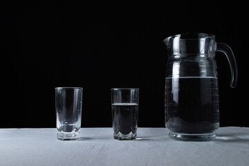 Decanter with water on a black background. A decanter and a glass filled with water, next to an empty glass. Clean drinking water. Ecology cleanliness concept.