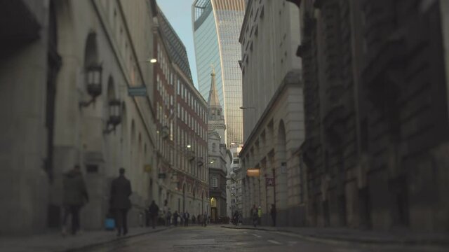 A narrow street in London with old massive buildings and pedestrians