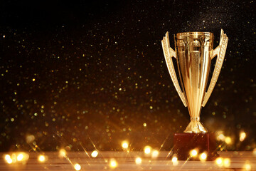 image of gold trophy over wooden table and dark background, with abstract shiny lights
