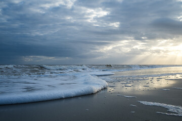 Fototapeta premium Sunset at the Beach with Sunbeams and Foam in the Water