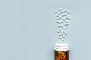 White scattered pills in the shape of a heart and a jar with dark glass on a blue background.