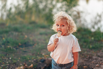 The little blonde girl is eating marshmallows. The child bakes sweetness at the stake.