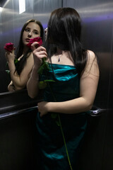 sexy confident brunette woman in elegant aquamarine colored dress with red rose in grey elevator