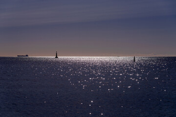 Beautiful peaceful seascape with small ship and lighthouse silhouette on the sea horizon