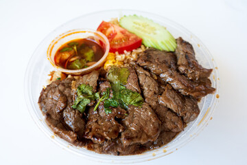 Asian dish prepared with beef pieces, tomatoes and cucumber slices on top of fried rice served in a bowl, for an healthy and complete meal