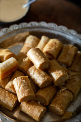 Traditional tahini crispy roll with bowl of tahini on wooden background. Dry Baklava with Tahini or Tahini Crispy.