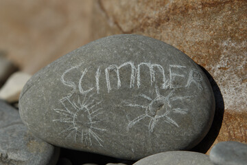the word summer on a stone on a sunny day on a pebbly sea beach written in chalk