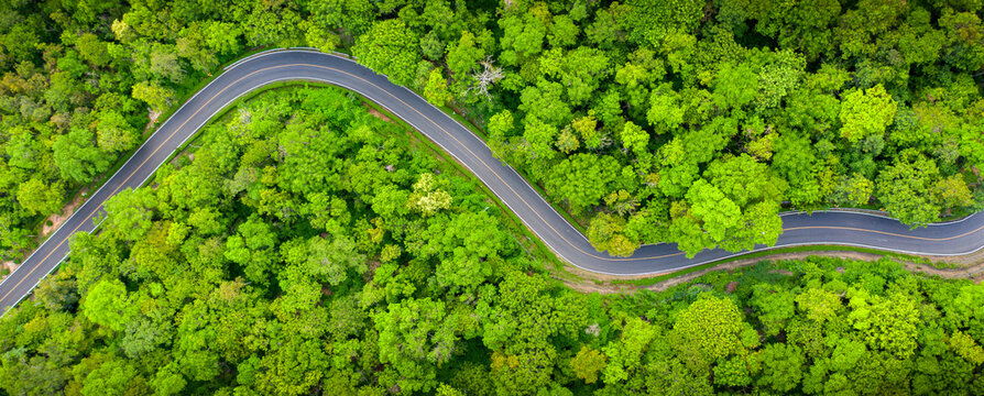Winding road, top view of beautiful aerial view of asphalt road, highway through forest and fields in rainy season. For traveling and driving in nature. Banner panorama background.