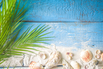 Summer Holiday Background. Old blue wooden plank table with seashell, starfish and beach sand, tropical leaves. Flatlay, top view copy space for your text. With photo frame and summer hat