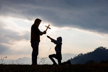 Silhouettes of father handing crucifix to daughter, Religion legacy concept