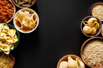 Different types of pasta in a bowls on a black background with copy space