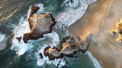 Vista aérea de olas que golpean las rocas en la playa y huellas de carro en la arena 