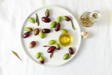 Fototapeta na wymiar Fresh green and black olives and a oil bowl on a plate over a linen tablecloth. A bottle of cold pressed oil is next to it. 