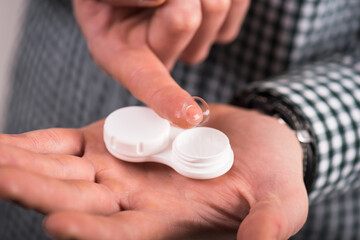 Close-up of a contact lens and a contact lens case held in the hand of a man in a plaid shirt.