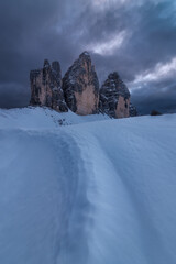 Trail in the snow in front of Tre Cime di Lavaredo, UNESCO heritage site in the Italian Dolomites, on a cloudy sunset