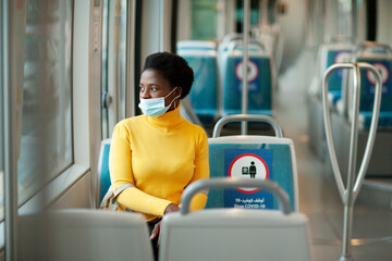 Dubai, UAE, November 2020 A young African woman wearing a protective mask rides on a bus and looks out the window. Coronavirus, social distance