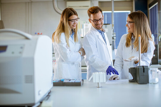 Researchers In Protective Workwear Standing In The Laboratory And Analyzing Liquid Samples At Ion Chromatography Equipment