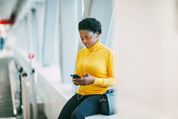 Attractive African girl is waiting for a train in the subway and listening to music with headphones