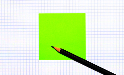 On a piece of checkered paper there is a green note sticker and a black pencil. Copy space