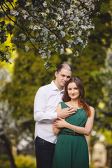 Fototapeta premium Young man and woman couple in a blooming apple garden. Tender holding each other. Spring lovestory. Brown-haired girl with long hairs. Young family