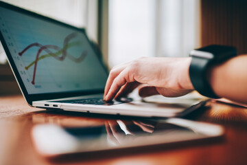 Obraz premium Faceless man typing on laptop and making graphs