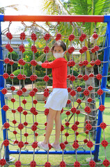 Asian little girl wearing a protective mask while playing on climbing rope net outdoor. Rear view