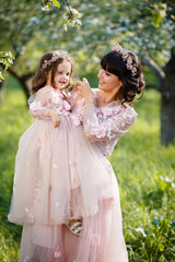 Fototapeta na wymiar Mother and little daughter hugging in blooming apple garden. Mom loves her child. Spring story. Family look romantic similar dresses. Happy family in beautiful spring day