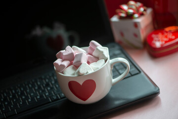 Large mug cup hot chocolate coffee with marshmallows  sweets and red heart on black laptop keyboard