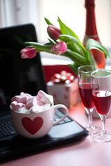 Large mug hot chocolate with marshmallows and two glasses red wine on black laptop keyboard