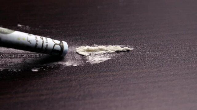Dolly moves from left to right along a line of cocaine powder sniffed up by a rolled-up dollar bill on a dark countertop. The concept of addiction and substance abuse