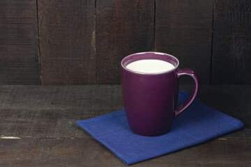 Purple cup of milk on blue cloth on brown wooden background. Dark tone.