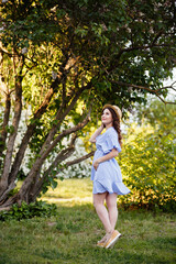 Young pregnant woman in spring lilac blooming garden. Romantic look with straw hat. Caucasian woman with long brown hairs. Concept of new life of nature and human. Waiting of baby