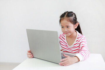 Pretty asian little child girl sitting at desk and using laptop computer stay at home