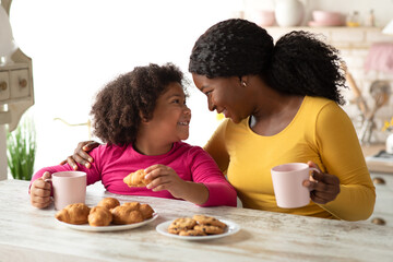 Loving Black Mom And Little Daughter Having Snacks In Kitchen At Home