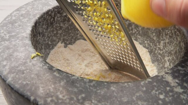 Close-up of the lemon grating on the grater into the grey stone mortar