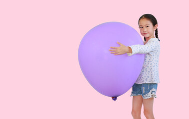 Portrait of asian little girl hug a big purple balloon with looking at camera isolated on pink background with copy space.