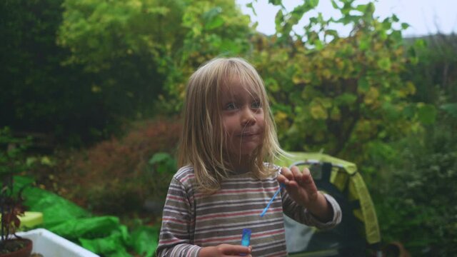 A little preschooler is blowing bubbles in the garden on an autumn day