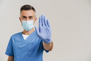 Serious medical doctor in face mask and gloves showing stop gesture