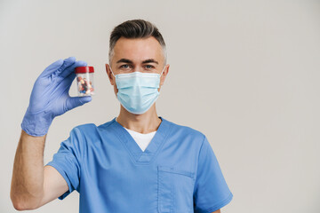 Happy medical doctor in face mask and gloves posing with capsules