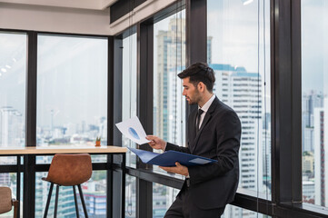 Fototapeta premium Caucasian businessman in suit standing with holding paperwork and analysing of business plan in the office