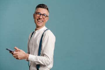 Happy grey-haired man in eyeglasses smiling and using cellphone