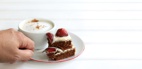 hand with a spoon separates a piece of chocolate and strawberry cake on the background of a cup with coffee. tasting sweet dessert
