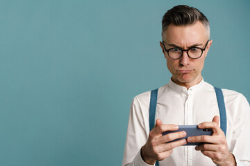 Shocked grey-haired man in eyeglasses playing online game on cellphone